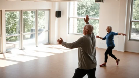 Zwei ältere Menschen machen Dehn- oder Tanzübungen in einem hellen Raum mit großen Fenstern.