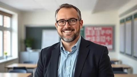 Lächelnder Mann mit Brille und dunklem Blazer in hellem Klassenraum mit Tischen.