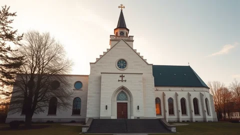 White church with tall steeple, cross, clock face, arched entrance on steps, side windows, green roof at sunset.
