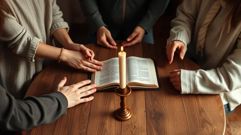 Hände mehrerer Personen ruhen um ein geöffnetes Buch, Kerze brennt daneben auf einem Holztisch.