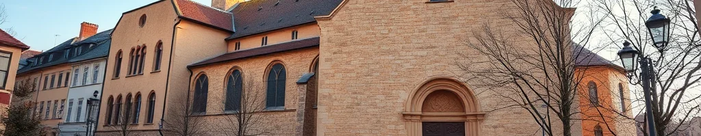 Straße vor einer großen Backstein-Kirche mit Turm und Kreuz; Menschen schlendern über den Vorplatz.